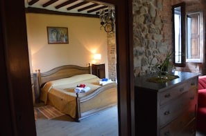A bedroom with a wooden bed, a stone wall, a nightstand with a lamp, and a dresser with a mirror. - Podere San Lorenzo (Terranuova Bracciolini)