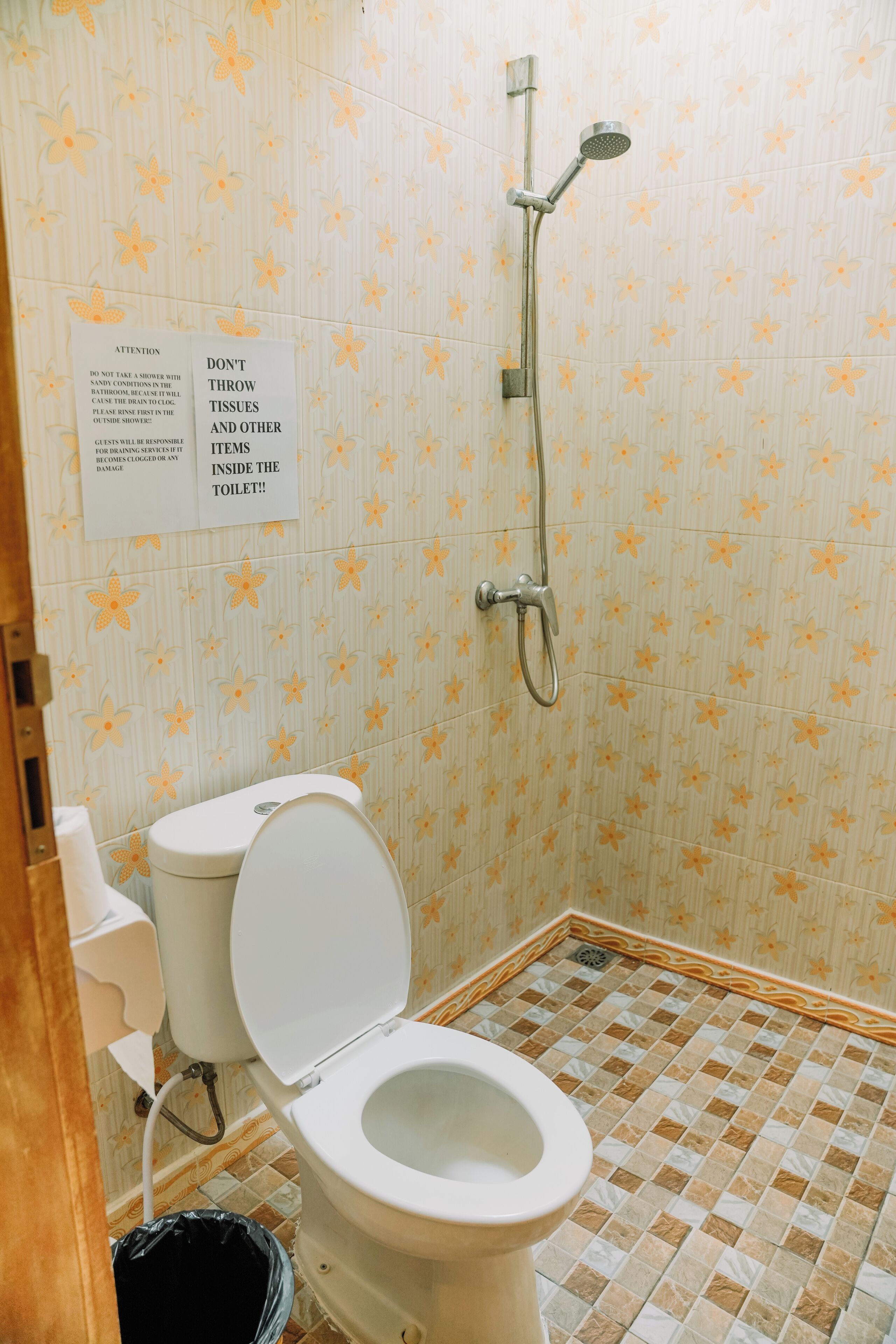A bathroom with a toilet, a shower, and a sign warning against throwing tissues and other items into the toilet.