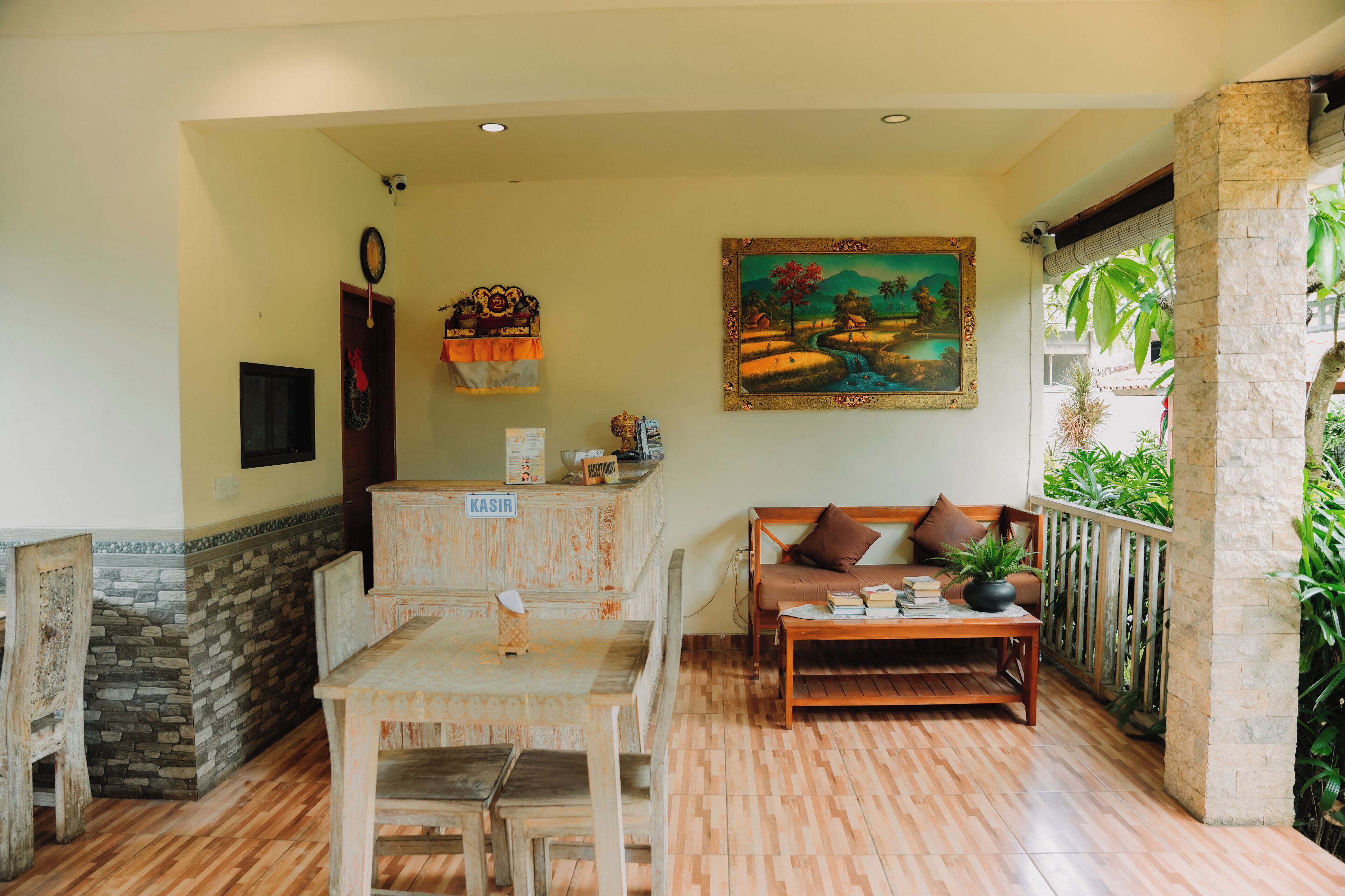 A cozy room with a wooden table, a sofa with cushions, a painting on the wall, and a stone wall.