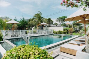 Une piscine entourée de verdure et d’une clôture blanche, avec des chaises longues et des parasols.
