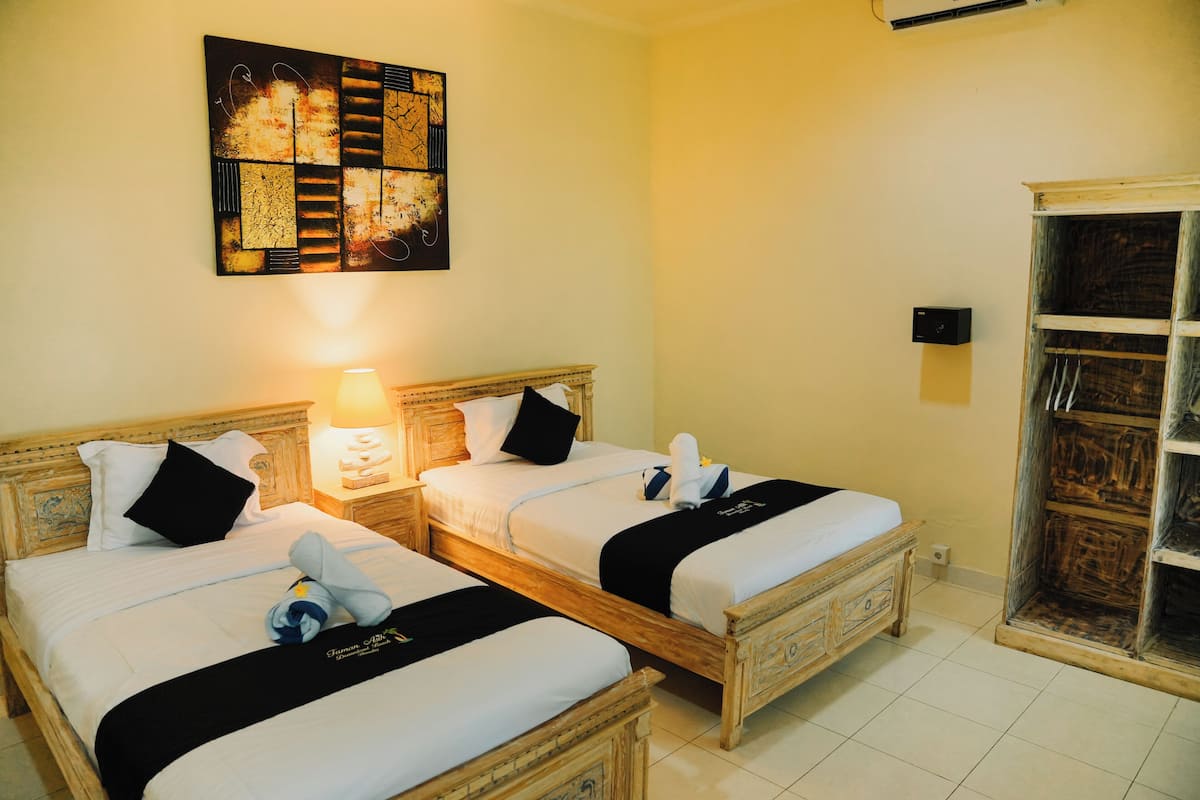 A hotel room with two wooden beds, a wall-mounted artwork, a bedside lamp, and a wardrobe.