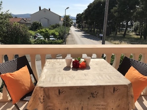 Ein Balkon mit Tisch, der mit einer Kaffeetafel bedeckt ist, zwei Stühlen und einer Vase mit Blumen.