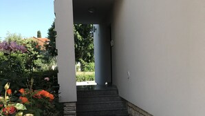 Un edificio moderno con un patio piastrellato, un muro in pietra e vista su un giardino con rose.
