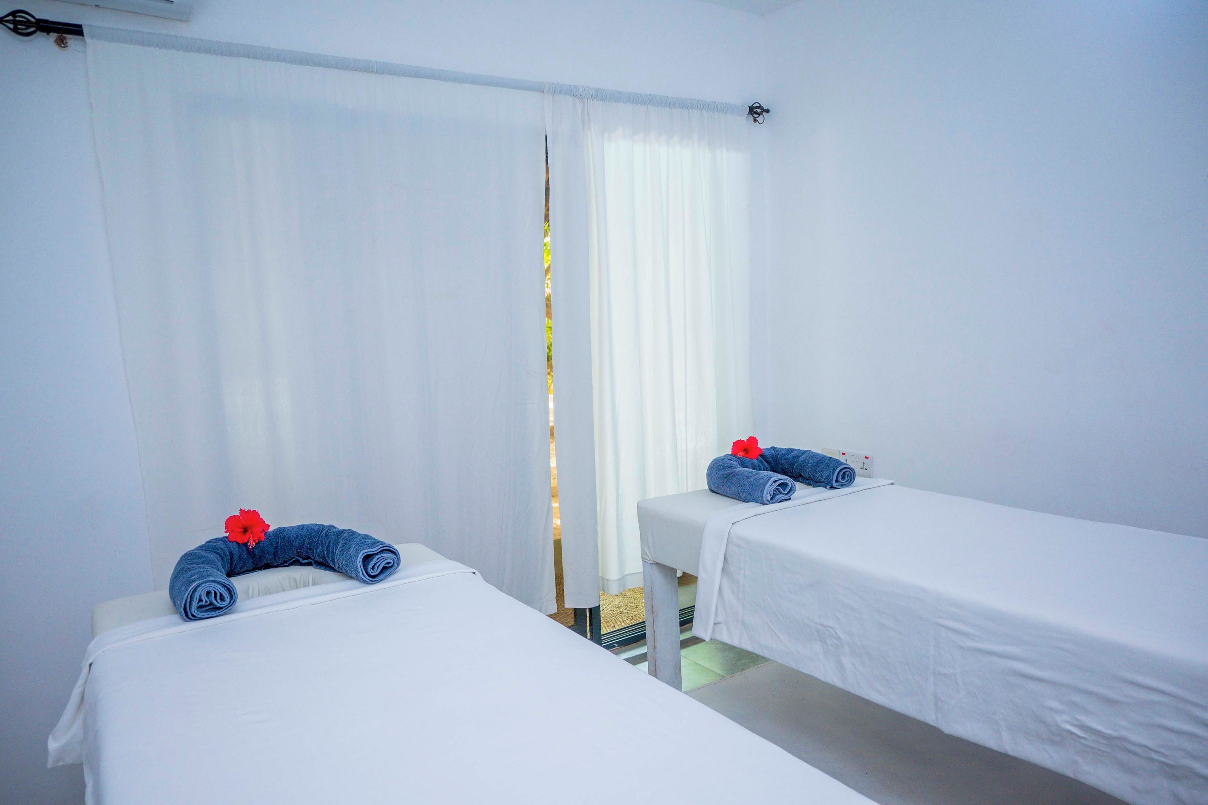 A hotel room with two single beds, white bedding, and a window with sheer curtains.