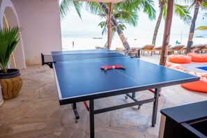 A ping pong table with a net, surrounded by stone flooring, palm trees, and beach chairs. - Sky & Sand Zanzibar (Matemwe)