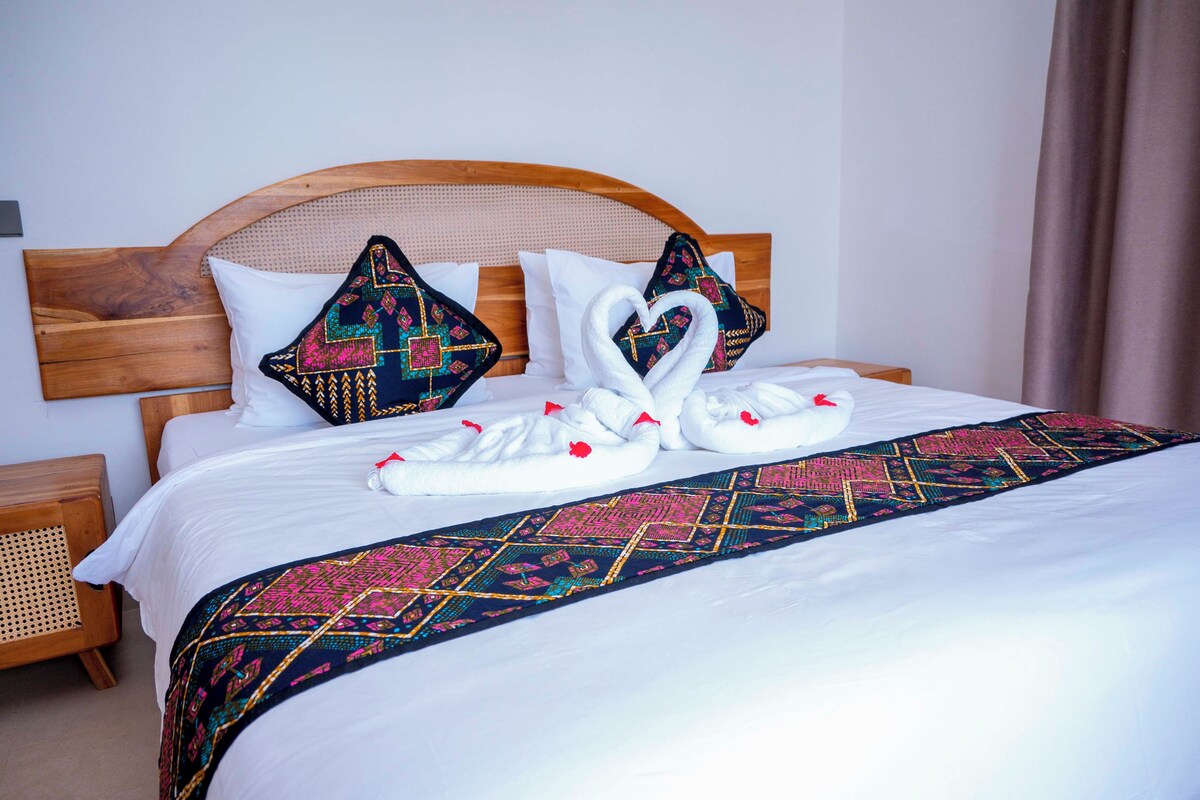 A neatly made bed with a decorative swan towel arrangement, a patterned bedspread, and a wooden headboard.