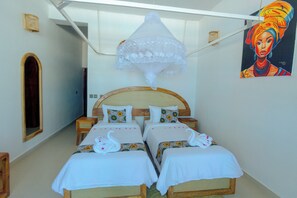 A room with two beds, a wooden headboard, a decorative hanging, and a painting on the wall. - Sky & Sand Zanzibar (Matemwe)
