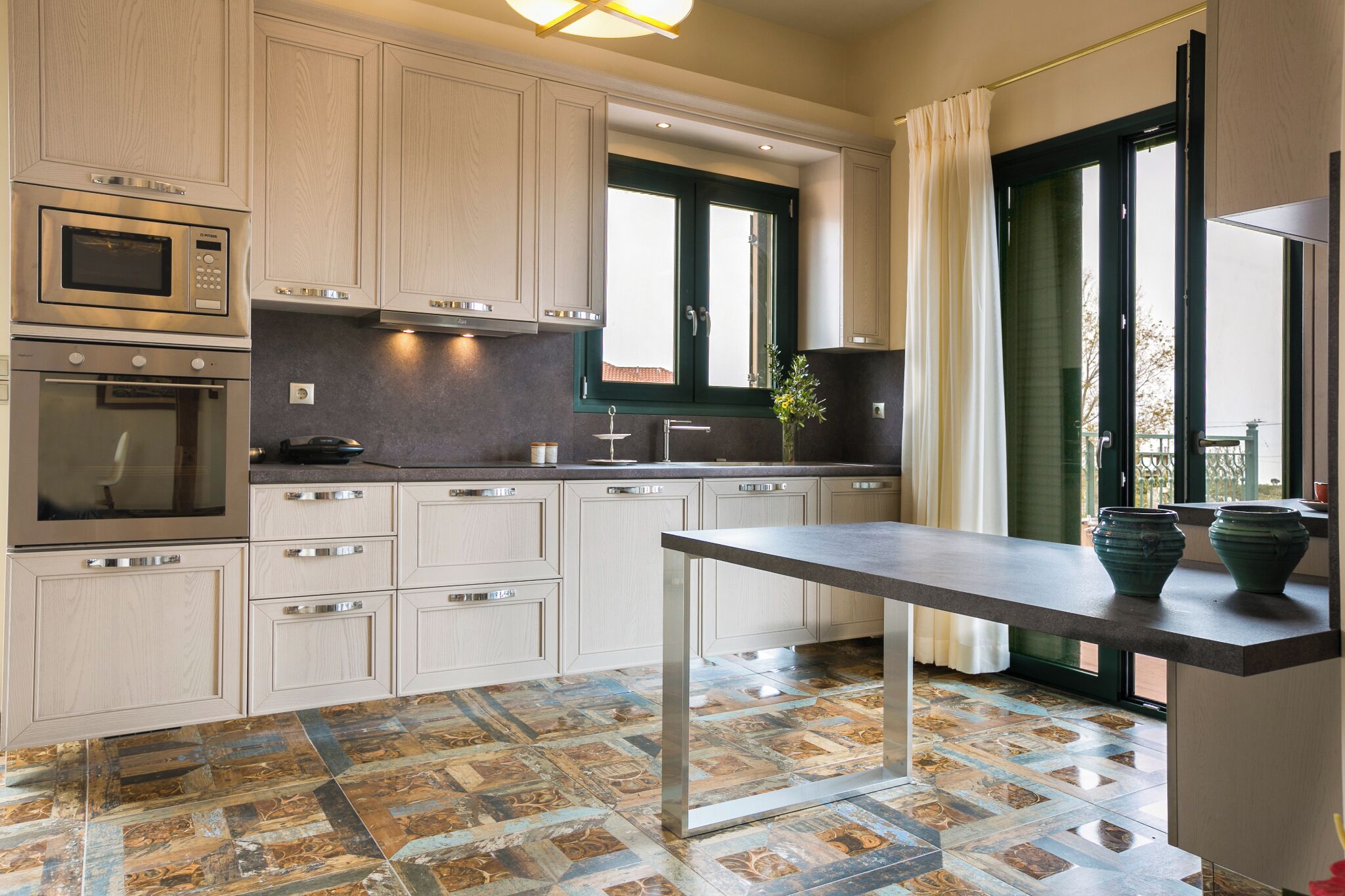 A modern kitchen with built-in appliances, a dining area, and large windows.