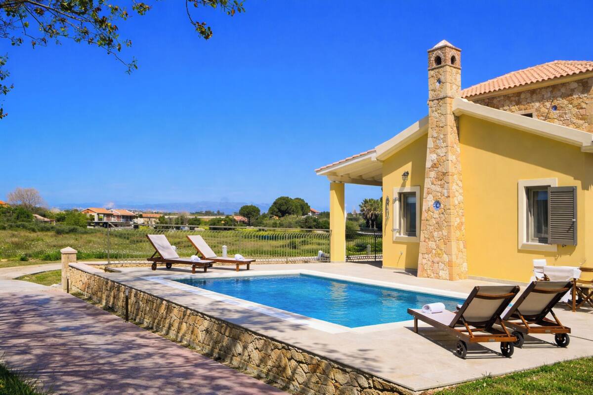 A poolside area with lounge chairs, a stone wall, and a view of the countryside.