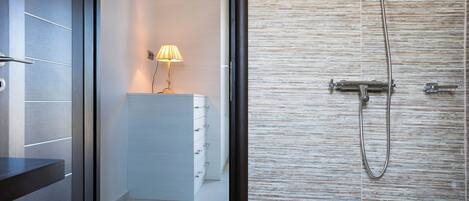 A modern bathroom with a shower, a white cabinet with drawers, and a lamp on the counter.