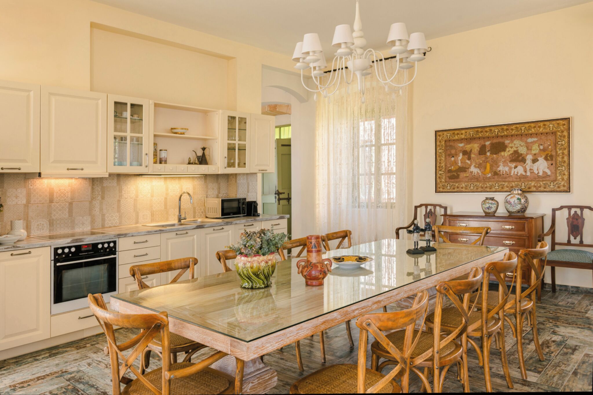 A kitchen with white cabinets, a glass dining table, wooden chairs, and a chandelier.