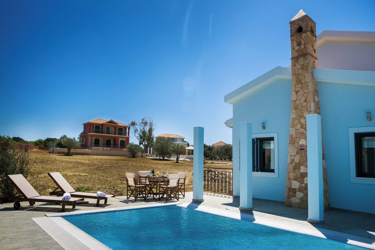 A pool area with lounge chairs and a table, a stone tower, and a building with a red roof in the background.
