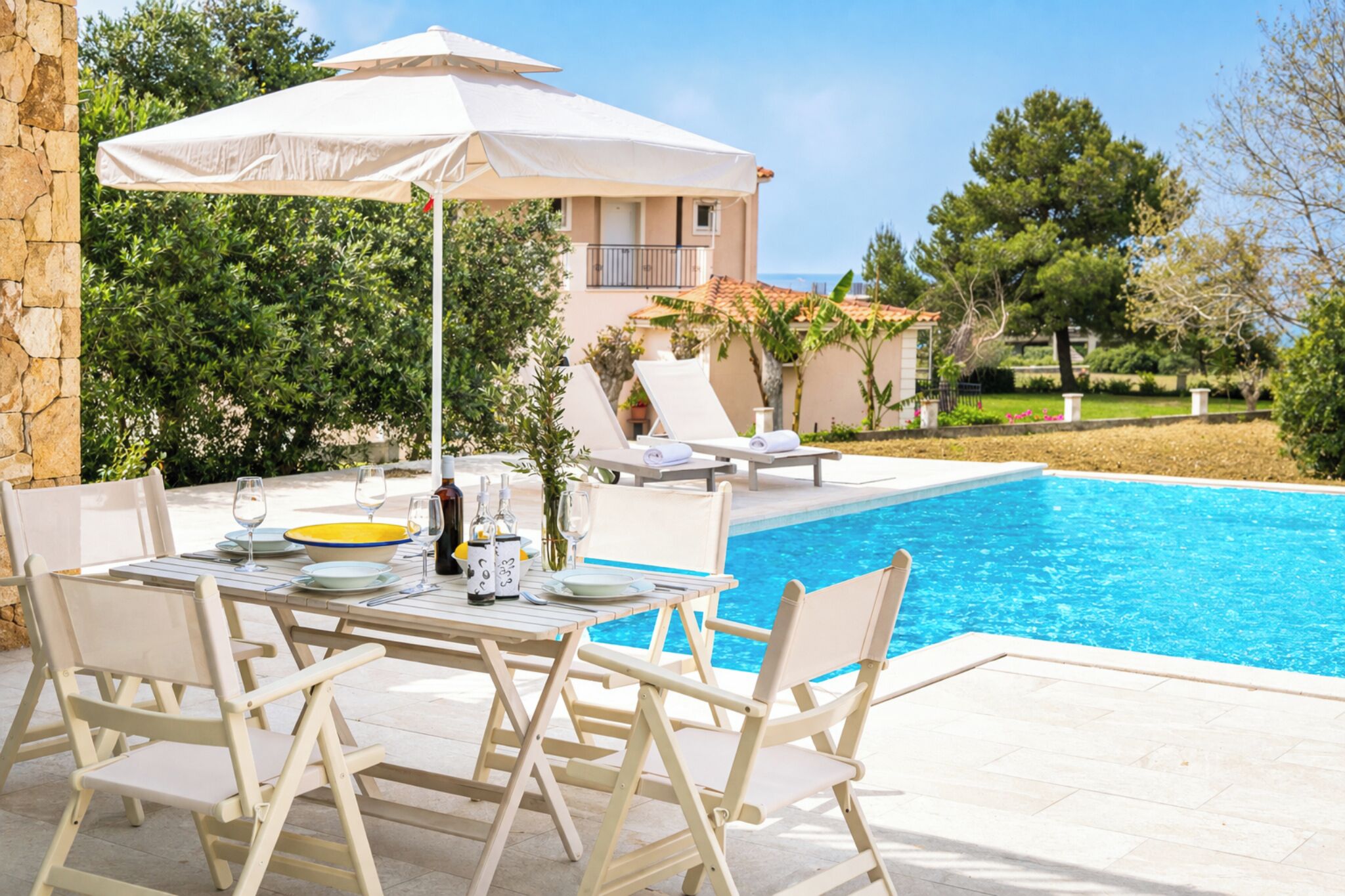 Un área de comedor junto a la piscina con una mesa para dos, una sombrilla blanca y una piscina.