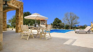 Area piscina con arco in pietra, tavolo e sedie, piscina e una poltrona prendisole.