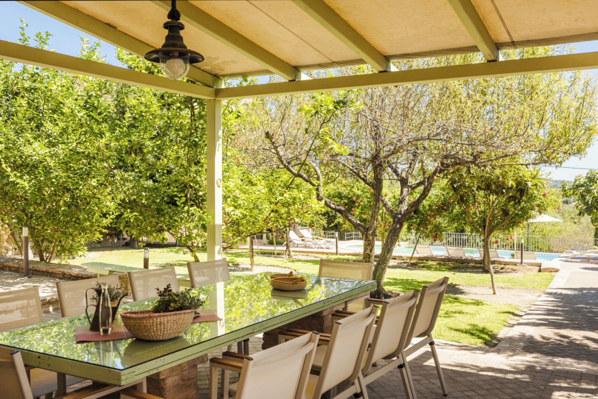 Un área de comedor al aire libre techada con una mesa de vidrio, sillas y una planta en maceta.