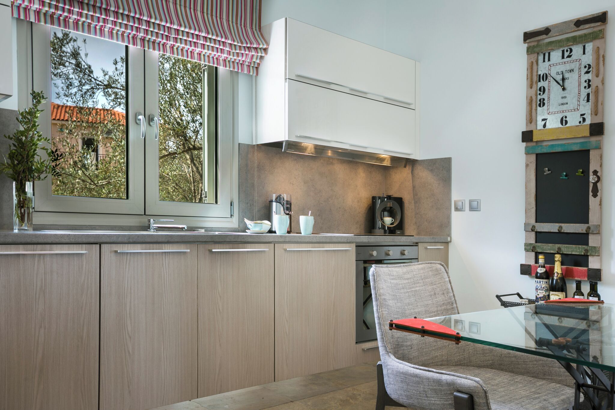 A modern kitchen with a glass table, a chair, and a clock on the wall.