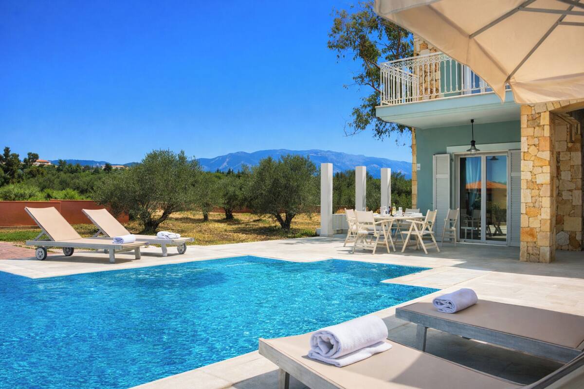 A pool area with lounge chairs, a table, and a view of mountains.