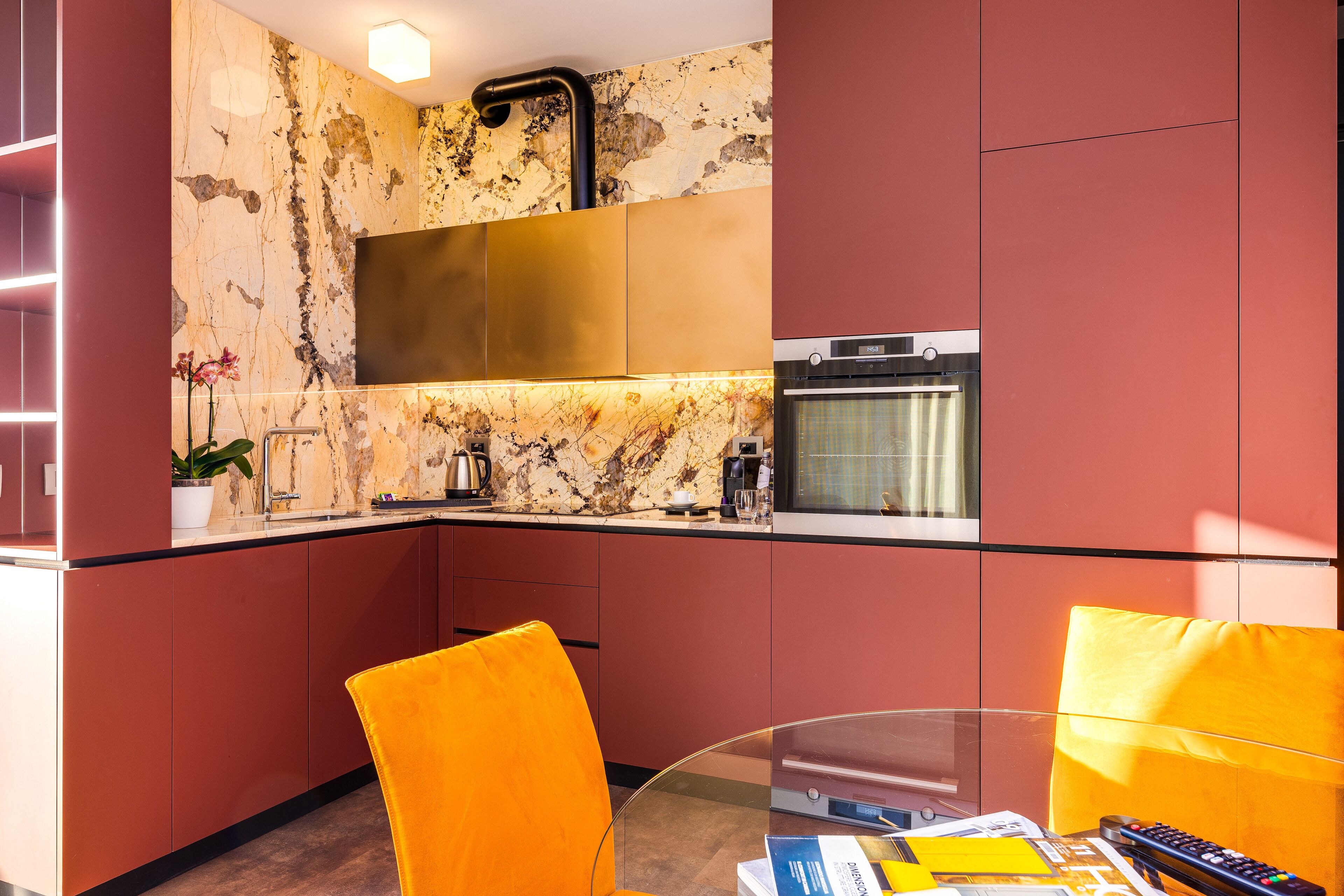 A modern kitchen with a marble backsplash, stainless steel appliances, and bright orange chairs.