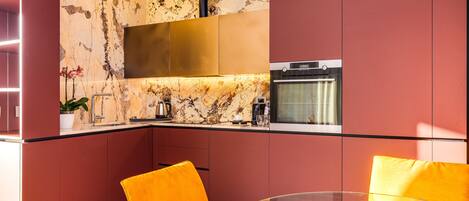A modern kitchen with a marble backsplash, stainless steel appliances, and bright orange chairs.
