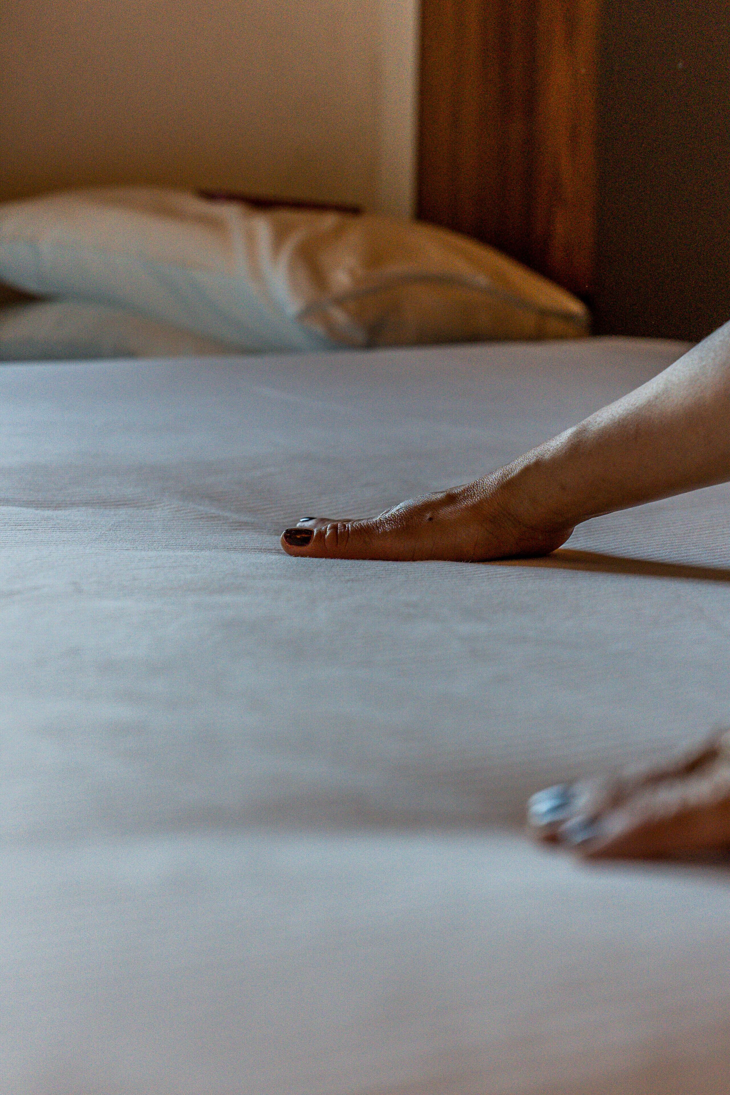 Primer plano de una mano que se extiende hacia una cama con sábana blanca.