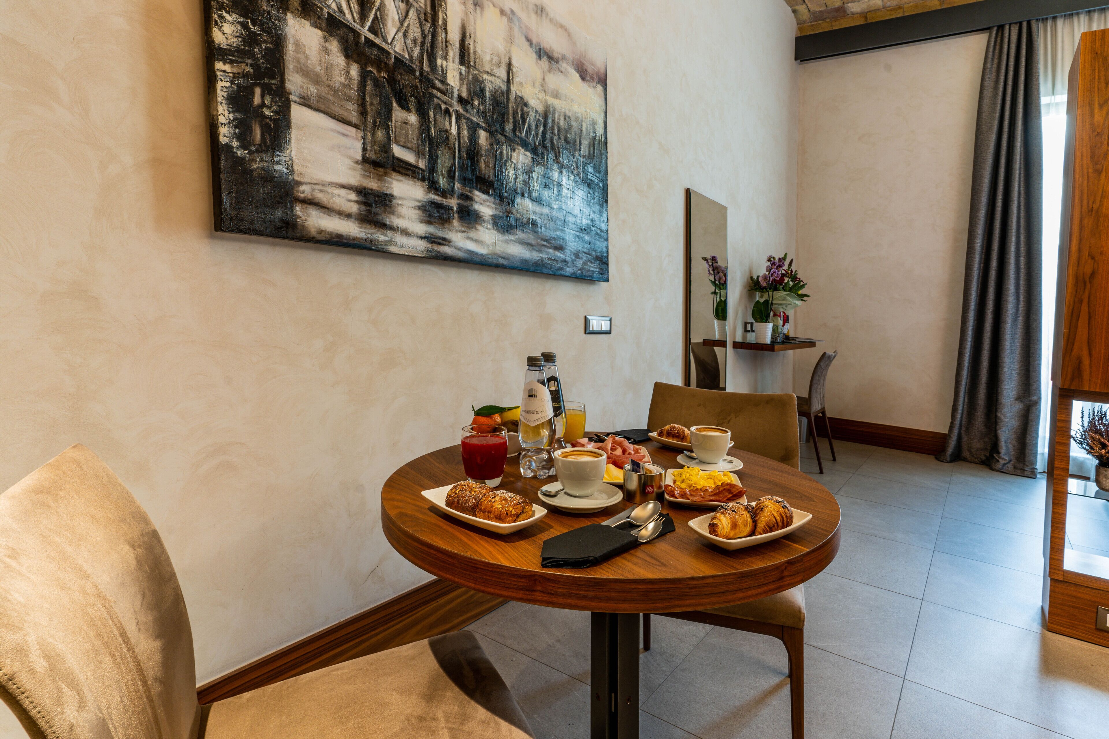 A dining area with a wooden table set for breakfast, including croissants, coffee, and juice.