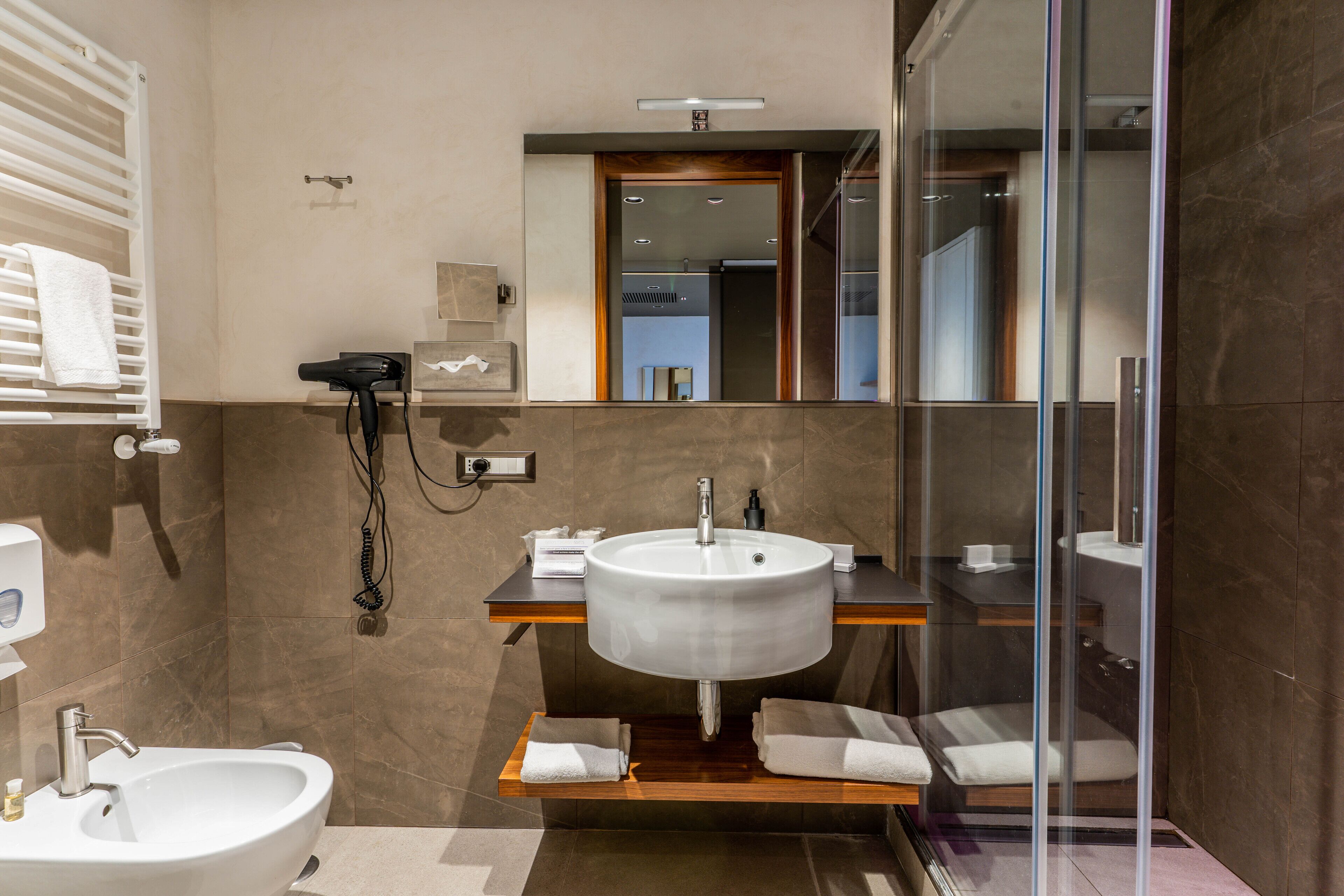 A modern bathroom with a large sink, a mirror, a glass shower enclosure, and a towel rack.