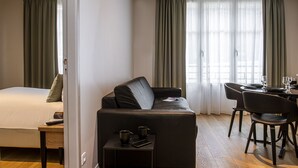 Habitación de hotel con cama, sofá, mesa de comedor con sillas y una mesita auxiliar con control remoto y taza.