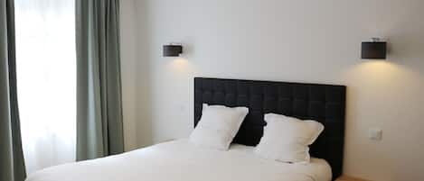 A neatly made bed with white linens and two pillows, a dark headboard, and two wall-mounted light fixtures.