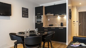 Una cocina moderna con armarios negros, horno empotrado y comedor con una mesa redonda y sillas.