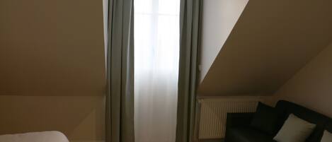 A room with a bed, a black sofa, and a window with curtains.