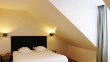 A bedroom with a high ceiling, a large bed with white linens, two bedside lamps, and a dark headboard.