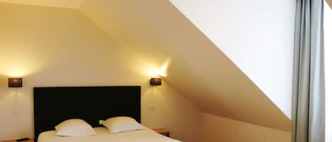 Un dormitorio con techo alto, una cama grande con ropa blanca, dos lámparas de noche y un cabecero oscuro.