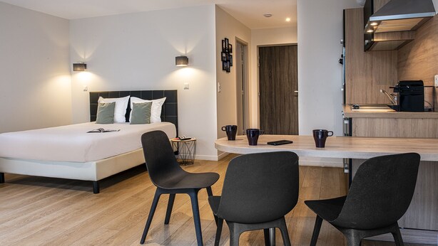 Una habitación de hotel moderna con una cama, dos sillas, una mesita y una kitchenette.