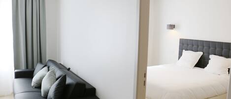 Habitación de hotel moderna con un sofá negro, una cama blanca y una cortina gris.