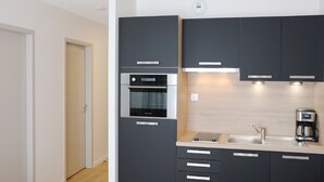 Una cocina moderna con armarios oscuros, horno empotrado, lavabo y cafetera.