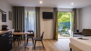 Habitación de hotel con cama, escritorio con cafetera, televisor y balcón con silla.