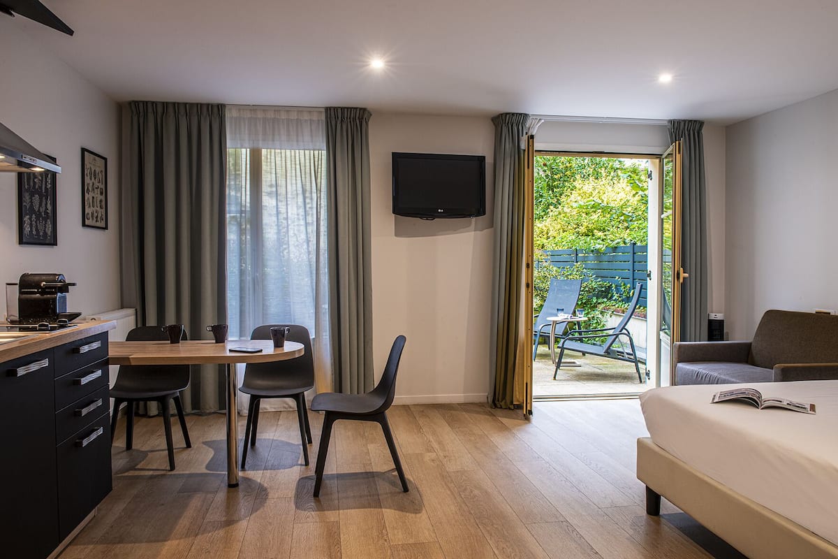 A hotel room with a bed, a desk with a coffee machine, a TV, and a balcony with a chair.