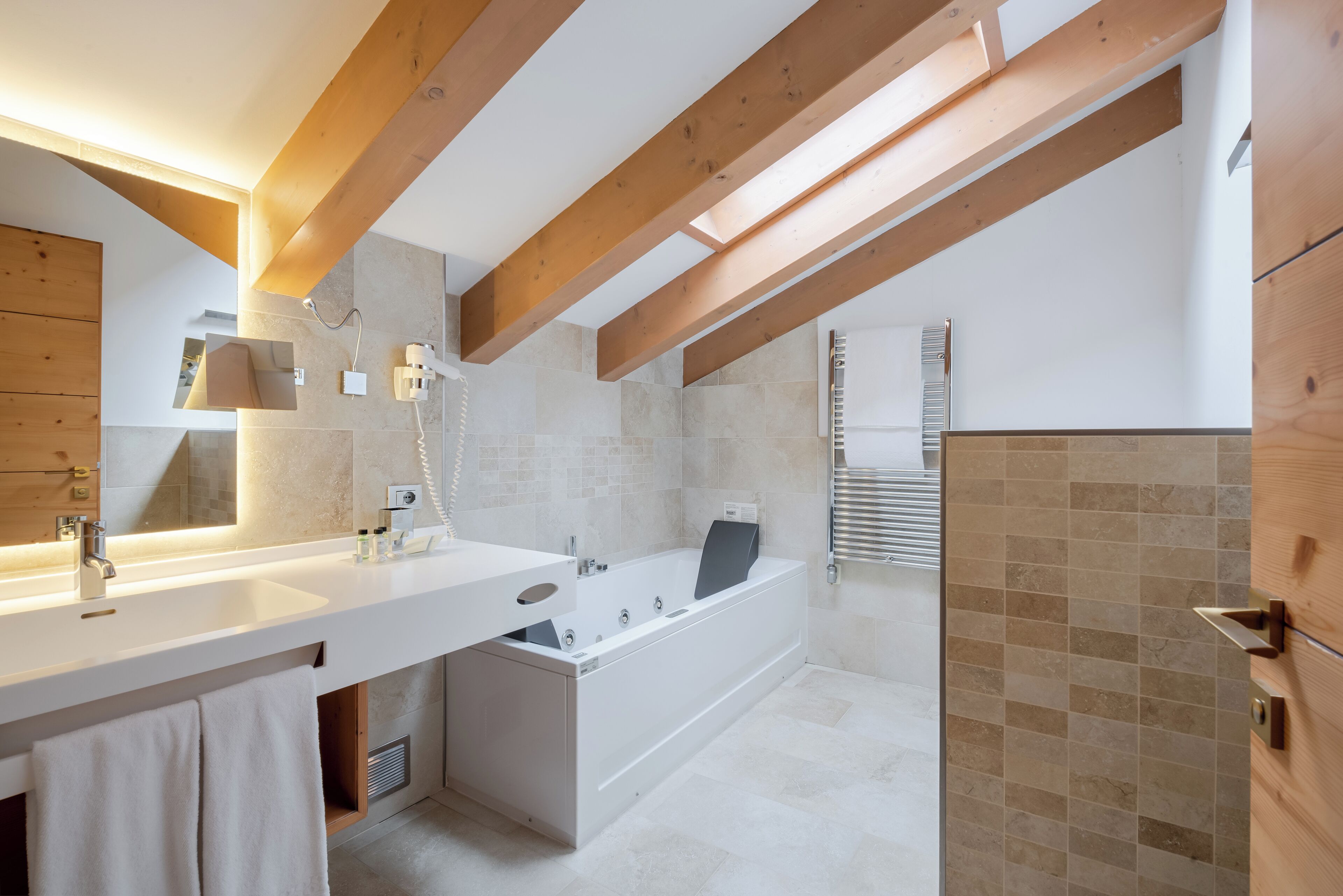 Une salle de bain moderne avec une grande baignoire, un meuble-lavabo à deux vasques et des poutres en bois au plafond.