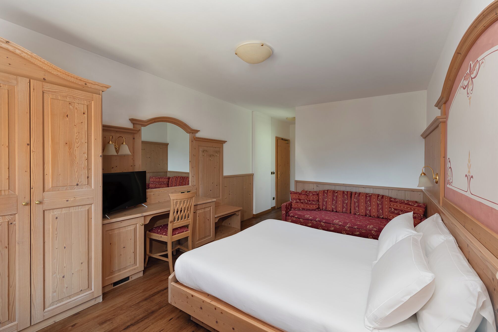 Een slaapkamer met een houten bed, een bureau met stoel, een televisie en een kledingkast.