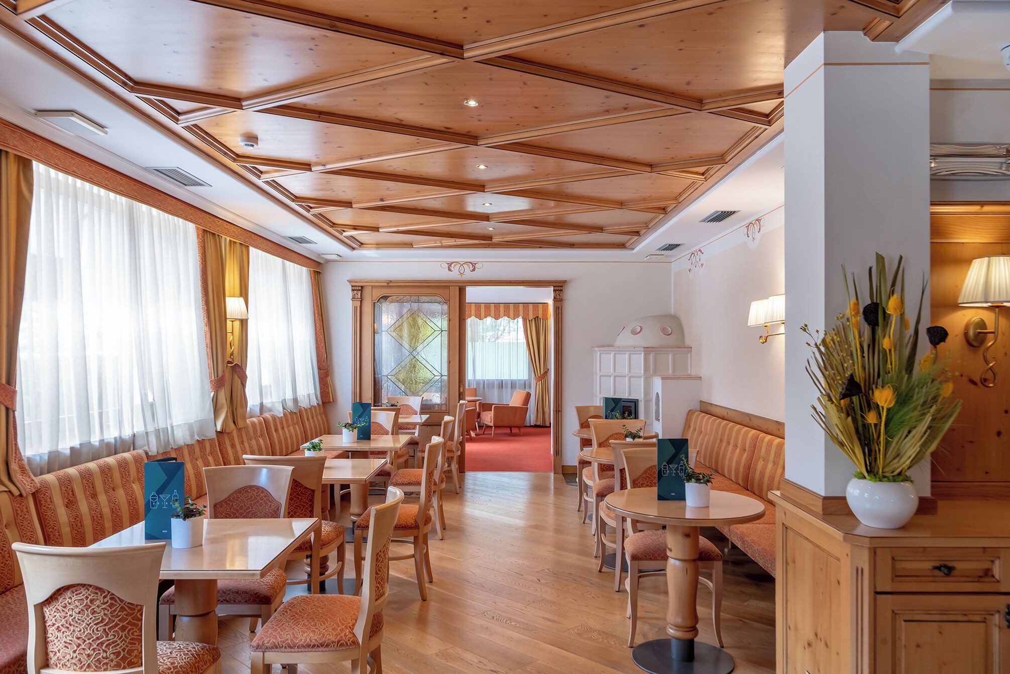 Un espace de restauration d’hôtel doté d’un plafond en bois, de plusieurs types d’aménagements pour s’asseoir et d’une cheminée.