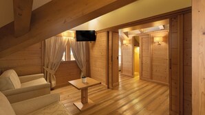 A cozy attic bedroom with wooden walls, a flat-screen TV, a small table, and a sofa. - Beverly Alps Hotel & Spa (Pinzolo)