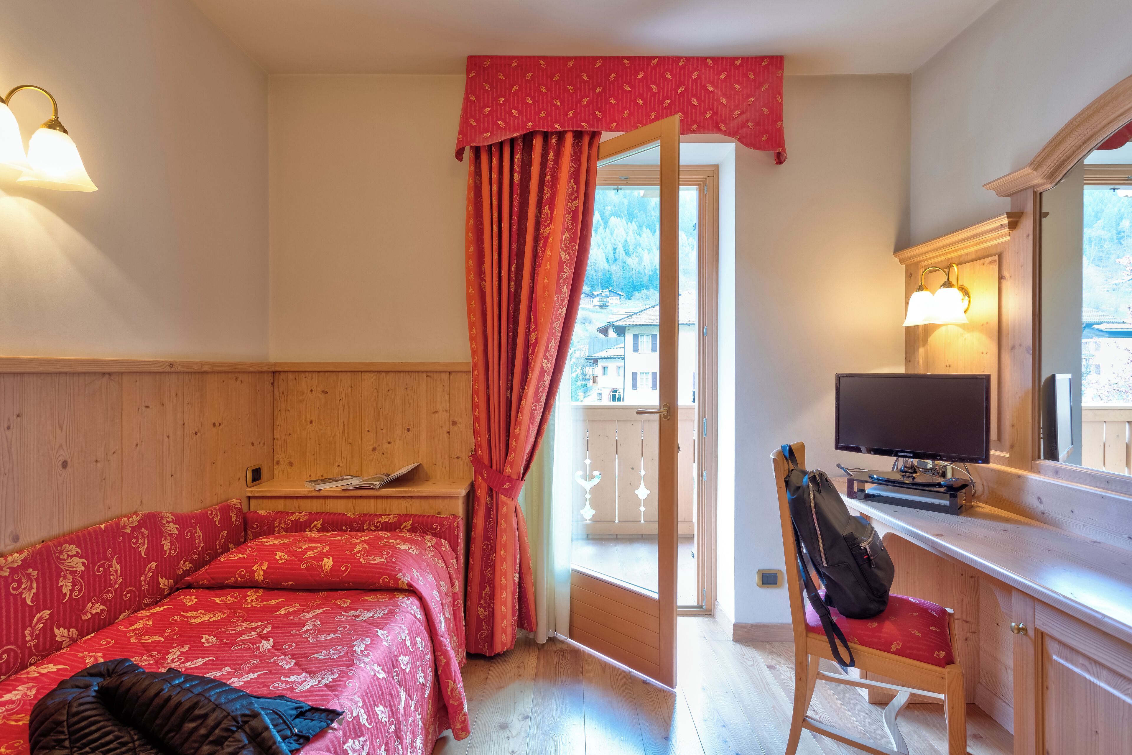 Une chambre avec un lit, un bureau avec un ordinateur et une fenêtre donnant sur des immeubles.