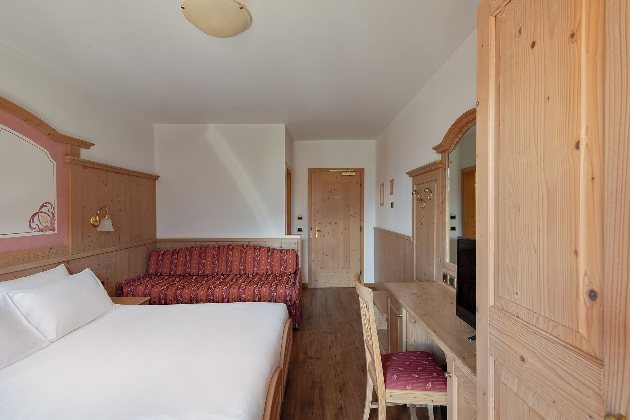 Une chambre à coucher avec un lit, un bureau et une chaise. Il y a une porte et un miroir sur le mur.