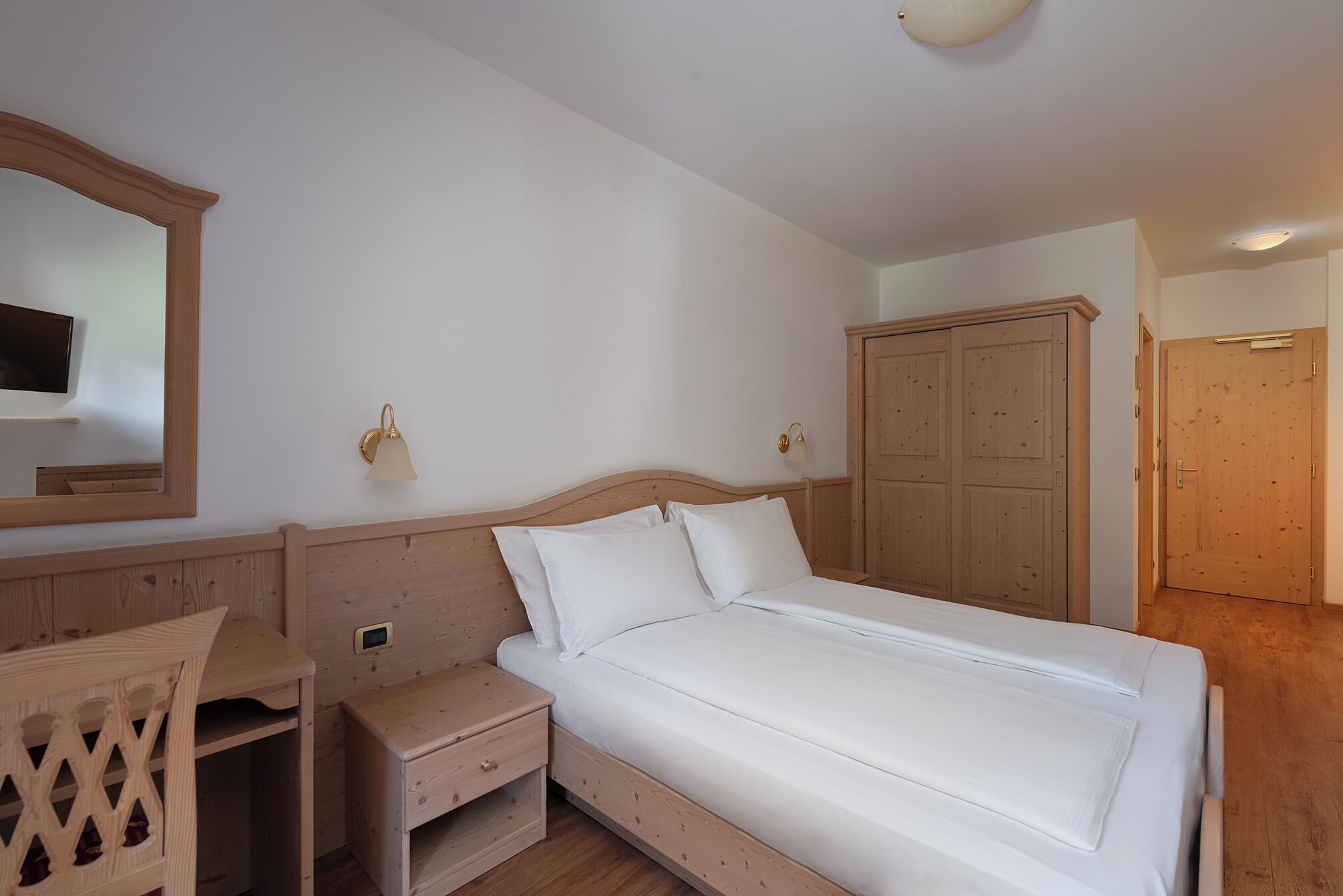 A bedroom with a wooden bed, a nightstand, a dresser, a mirror, and a wardrobe.