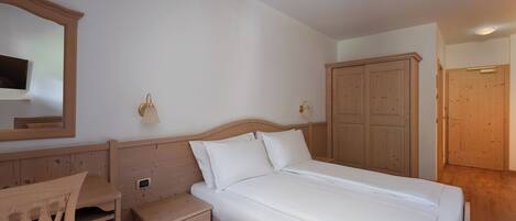 Quarto com cama de madeira, mesa de cabeceira, cômoda, espelho e guarda-roupa.