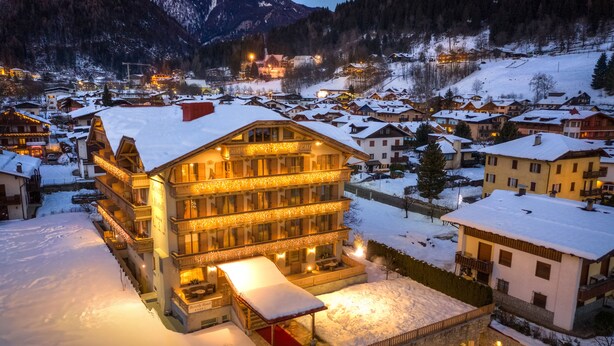 A multi-story hotel with a snow-covered roof, illuminated balconies, and a red carpet leading to the entrance. - Beverly Alps Hotel & Spa (Pinzolo)