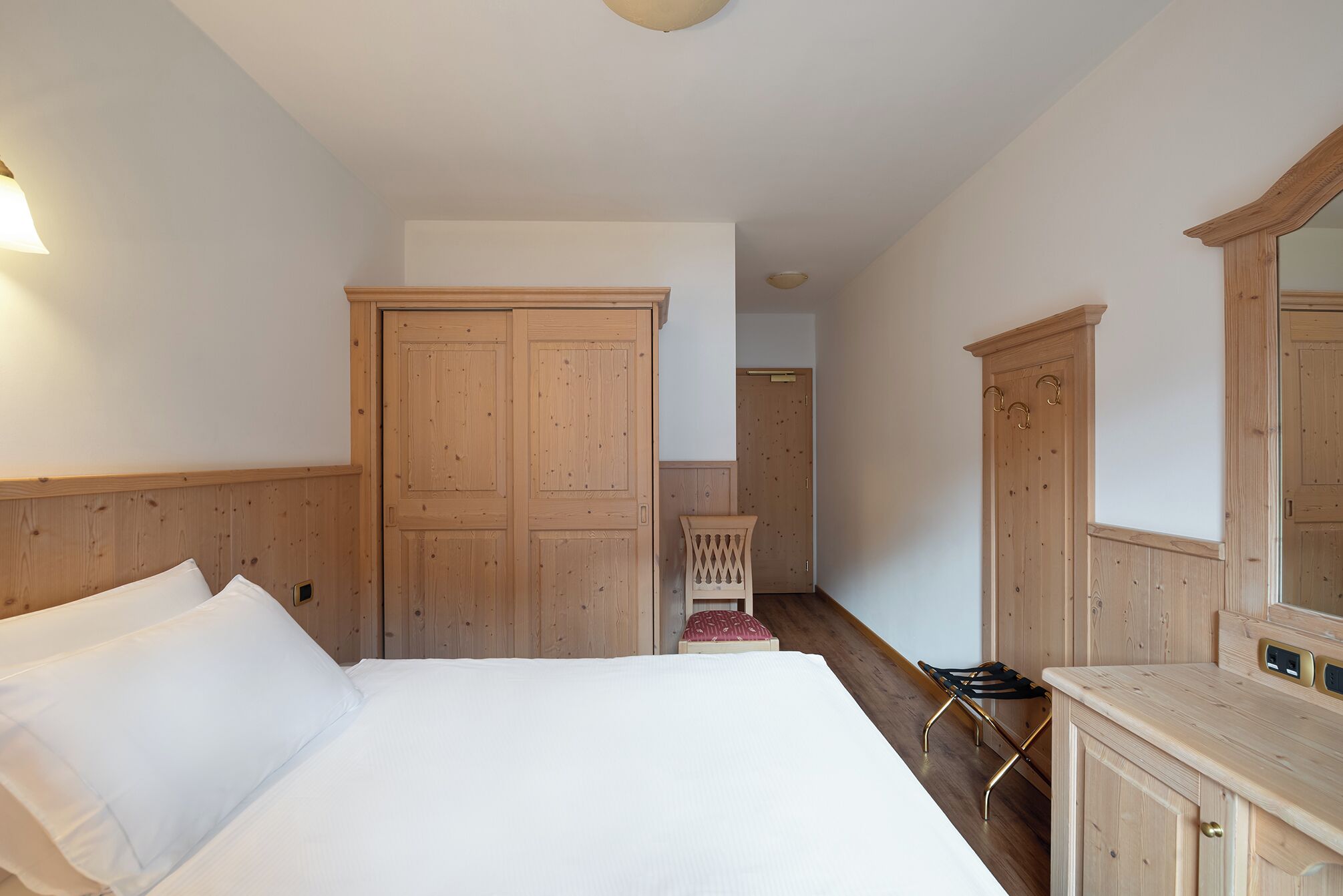 A bedroom with a large bed, wooden wardrobe, and a mirror cabinet.