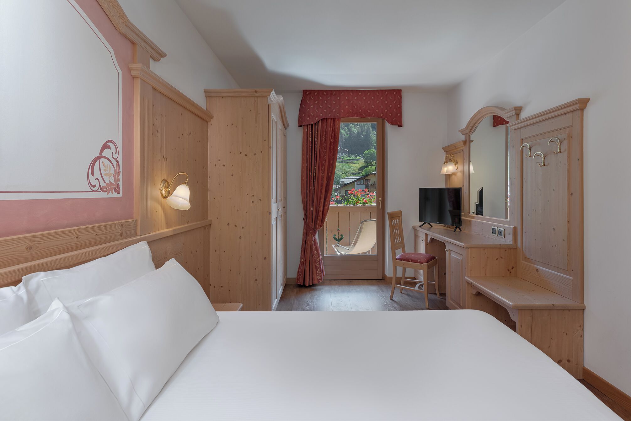 A hotel room with a bed, a desk with a TV, a chair, and a window with curtains.