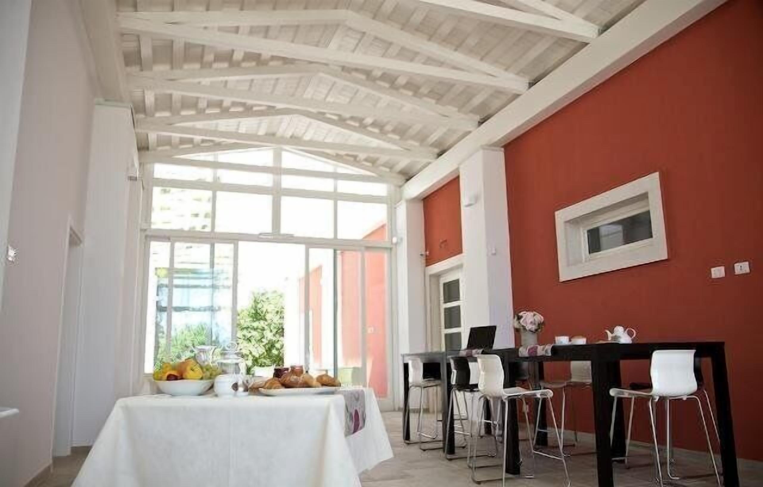 A dining area with a table set for two, a window with a view of greenery, and a red wall.