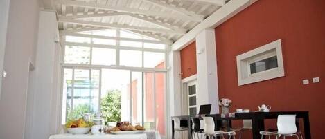 A dining area with a table set for two, a window with a view of greenery, and a red wall.